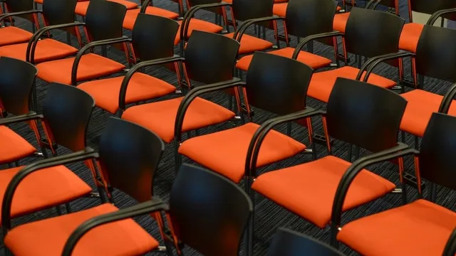 Des rangées de chaises orange et noires, vides, dans une salle de réunion.