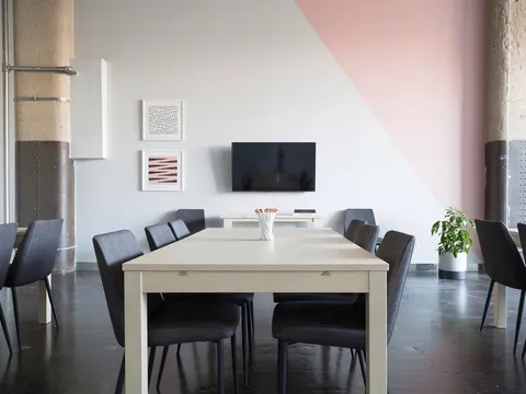 Une salle de réunion vide : une longue table claire et des chaises grises.