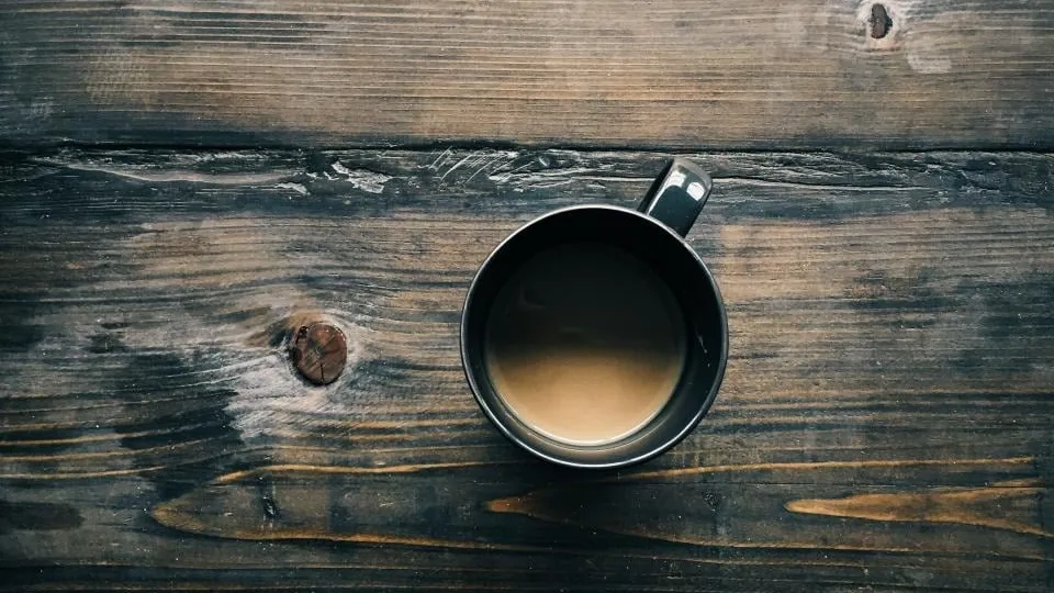 Une tasse de café posée sur une table en bois sombre, vue du dessus.